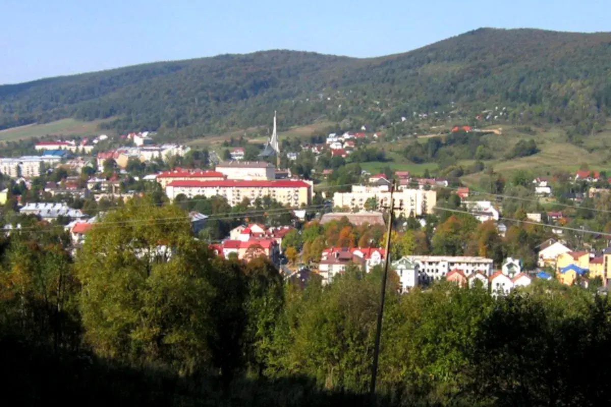 Widok na Ustrzyki Dolne z górami w tle. Miasto z czerwonymi dachami i nowoczesnymi budynkami, otoczone zielenią. Atrakcje turystyczne czekają!