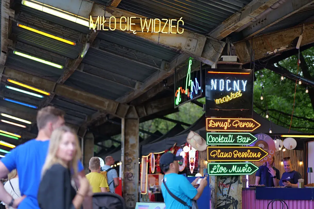 Nocny market Warszawa wita neonami: "Miło Cię Widzieć", "Drugi Peron", "Cocktail Bar", "Piano Sessions", "Live Music".