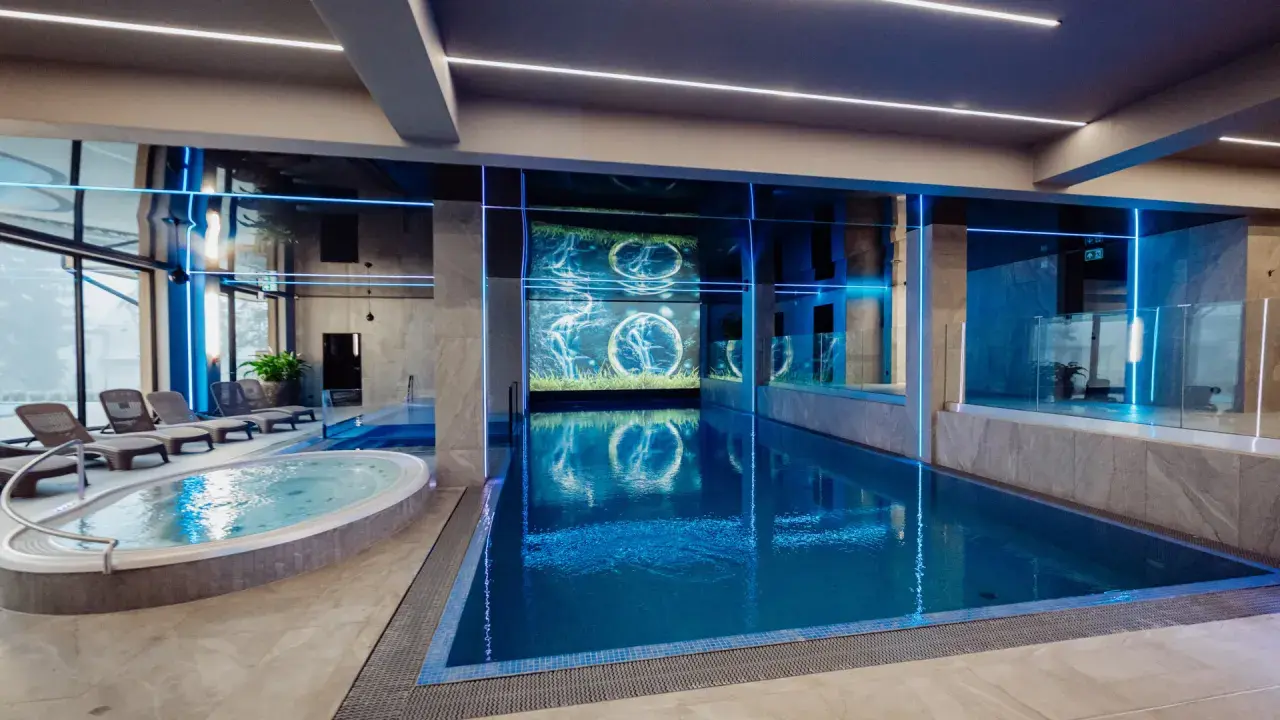 Nowoczesny basen i jacuzzi w rezydencji Aqua Szklarska Poręba. Niebieskie podświetlenie i ekran z animacją tworzą relaksującą atmosferę.