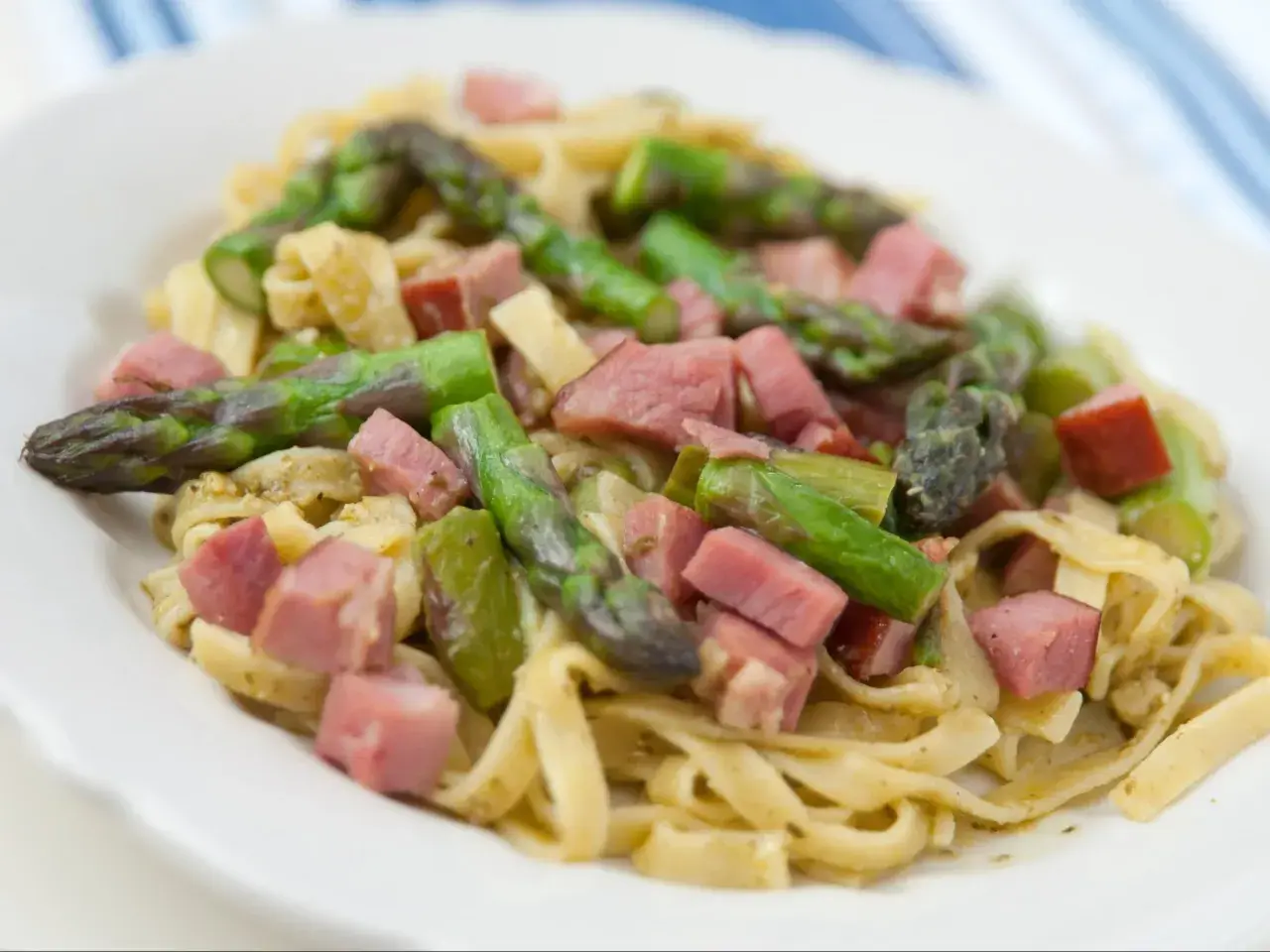 Pyszne spaghetti ze szparagami i kawałkami szynki na białym talerzu.