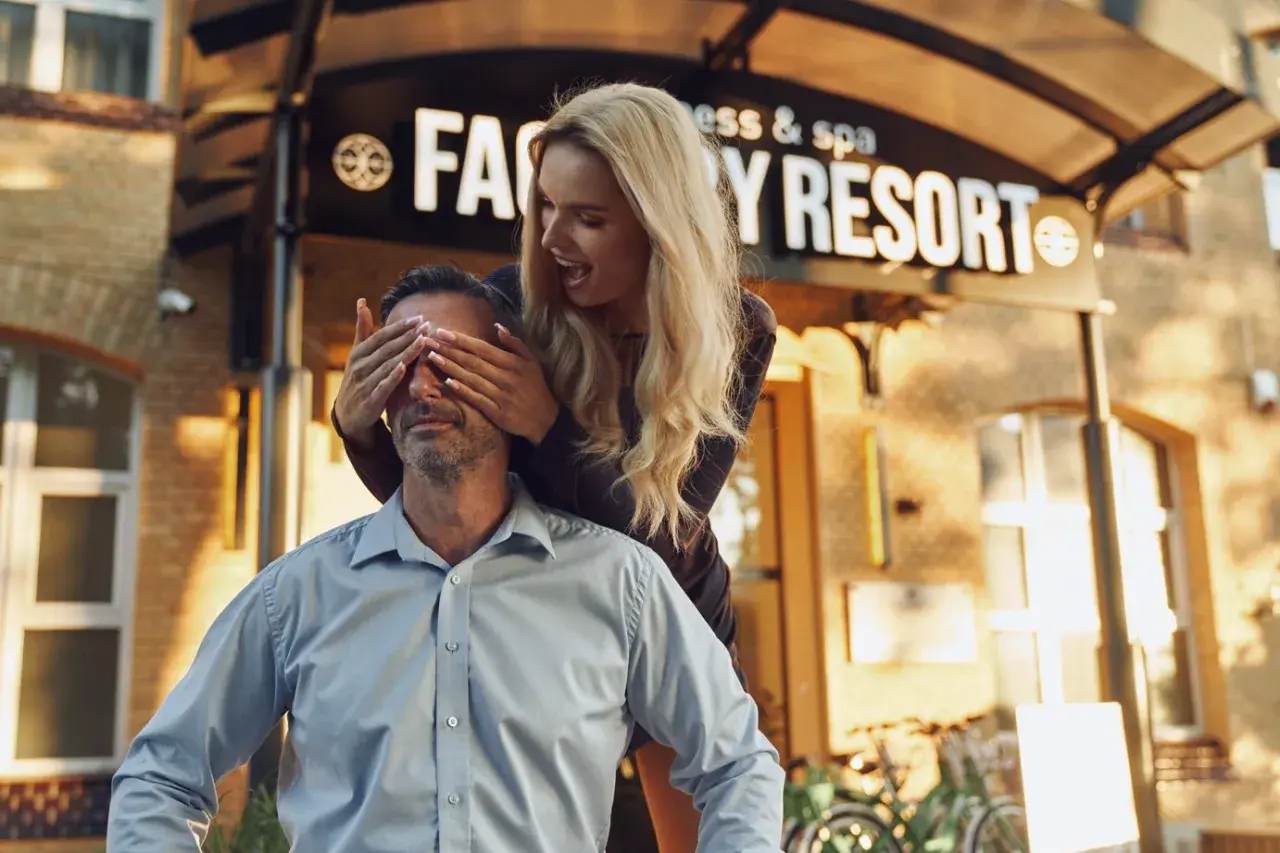 Zaskoczenie przed Factory Resort Kołobrzeg. Kobieta zakrywa oczy mężczyźnie, który uśmiecha się, czekając na niespodziankę.