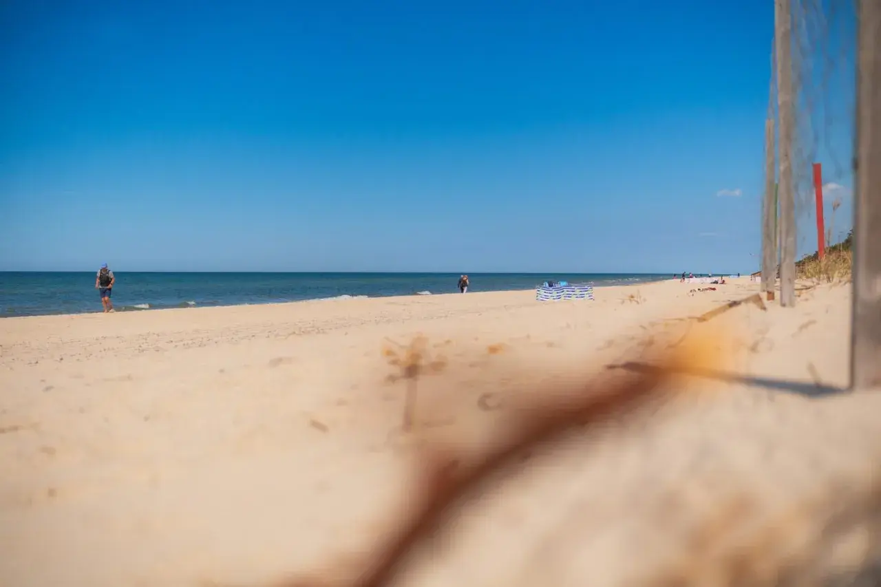 Słoneczna plaża w Niechorzu, idealne miejsce na relaks. W oddali widać ludzi spacerujących brzegiem morza.