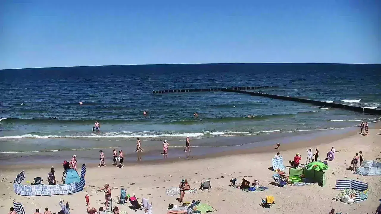 Słoneczna plaża w Dźwirzynie, ludzie kąpią się w morzu i odpoczywają na piasku. To jedne z wielu atrakcji tego miejsca.