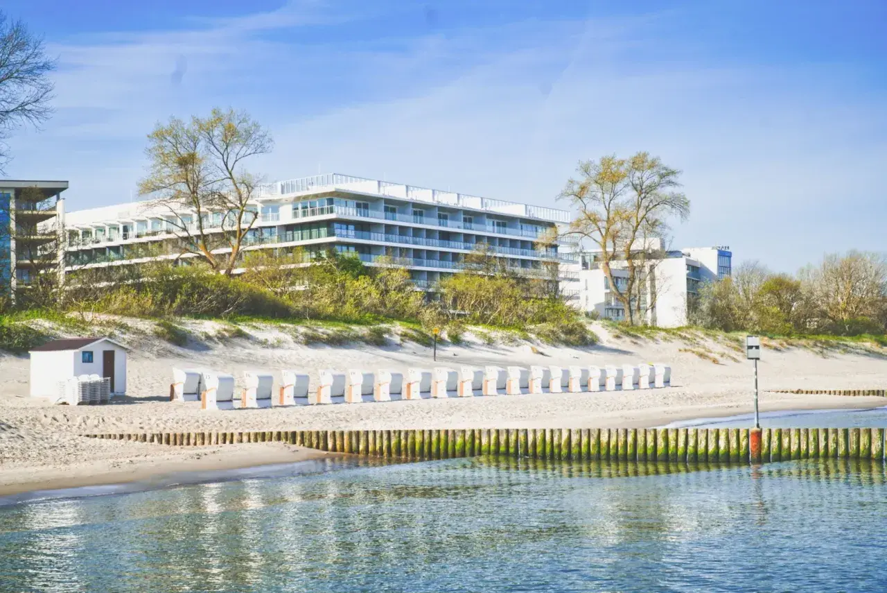 Nowoczesny seaside park hotel z widokiem na plażę i morze. Rząd białych leżaków plażowych czeka na gości.