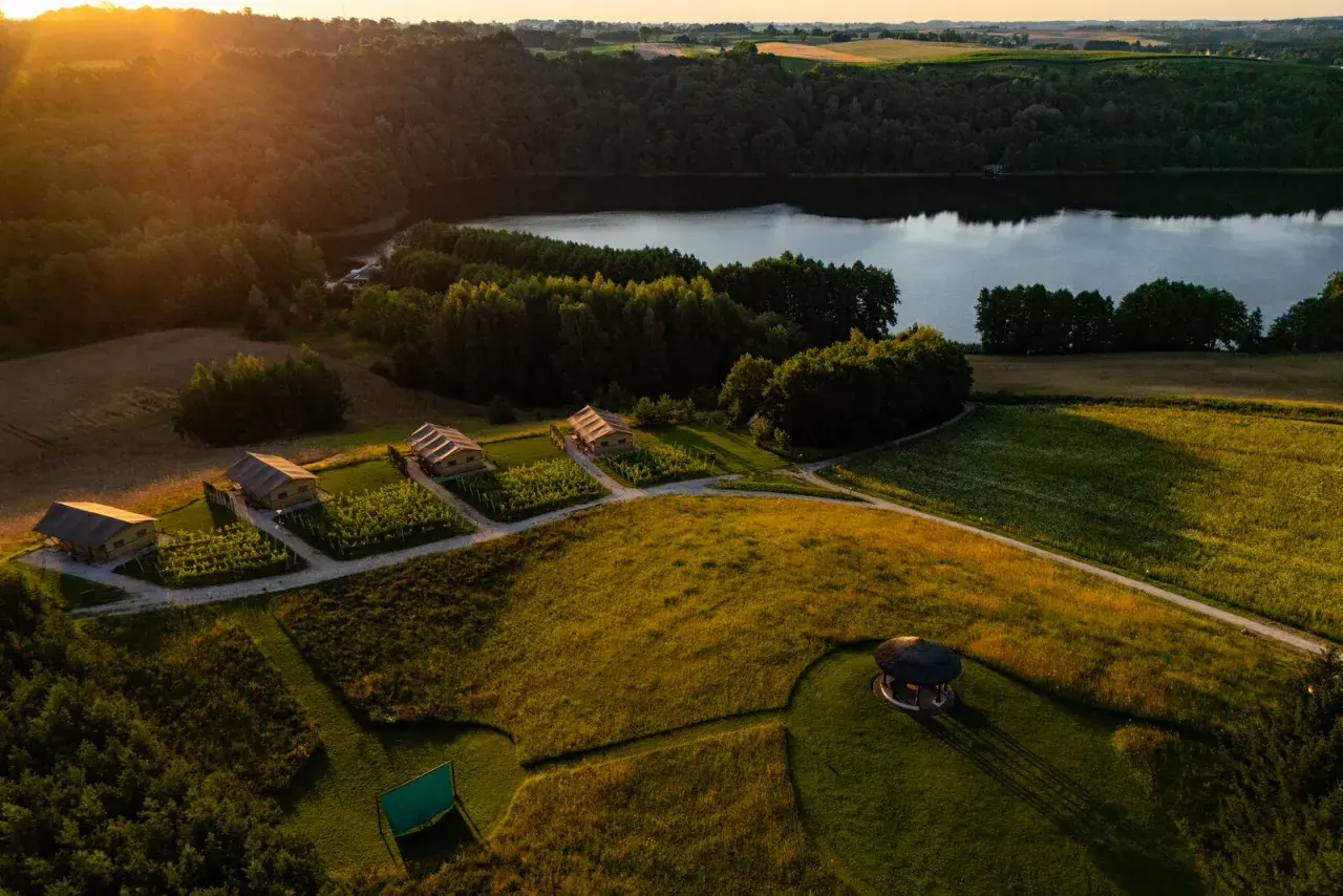 Malownicze domki nad jeziorem, idealne na tani wypad na weekend w Polsce. Złote słońce oświetla zielone pola i lasy.
