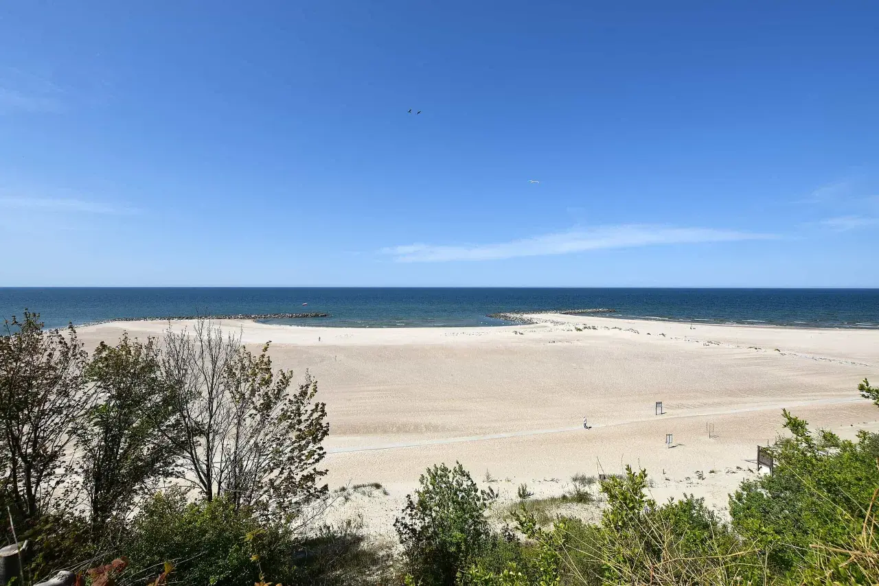 Szeroka, piaszczysta plaża w Jarosławcu, z łagodnymi falami Bałtyku i zielenią w tle. Idealne miejsce na relaks i podziwianie widoków, oferujące liczne atrakcje.