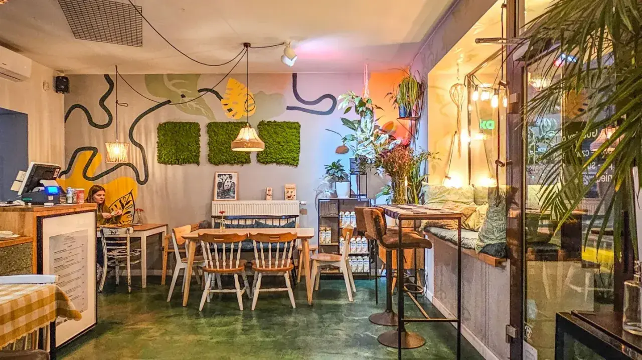 Wnętrze pełne zieleni i sztuki, tworzące przytulną atmosferę. Idealne miejsce na relaks w jednej z klimatycznych restauracji w Poznaniu.