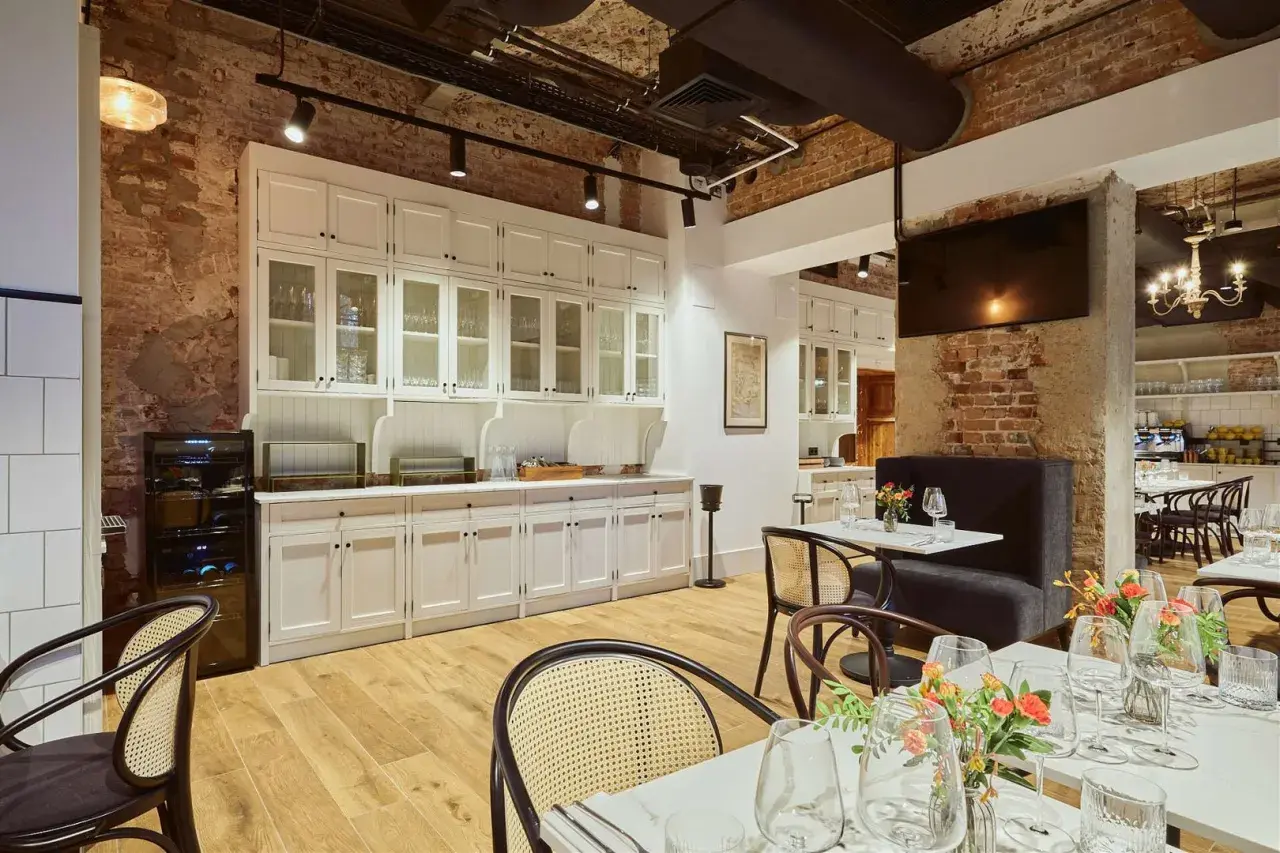 Eleganckie wnętrze restauracji Arche Klasztor Wrocław. Drewniana podłoga, ceglane ściany i białe meble tworzą przytulną atmosferę.