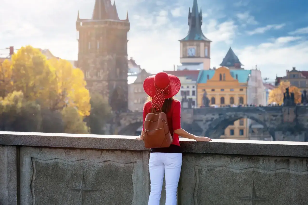 Kobieta w czerwonym kapeluszu podziwia praskie praga nietypowe atrakcje, w tym Most Karola i wieże.