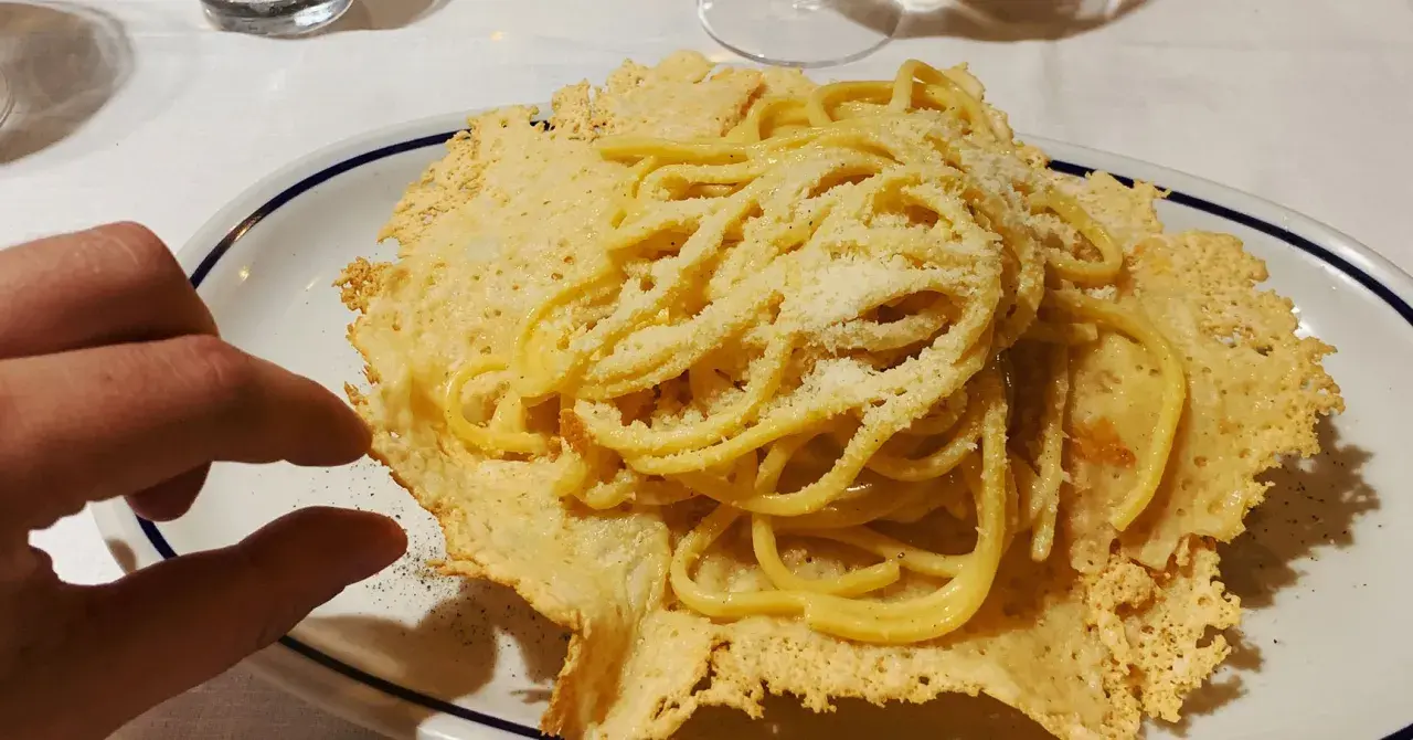 Pyszne spaghetti z parmezanem, podane na chrupiącym serowym "gniazdku". Idealna odpowiedź na pytanie: co zjeść we Włoszech.