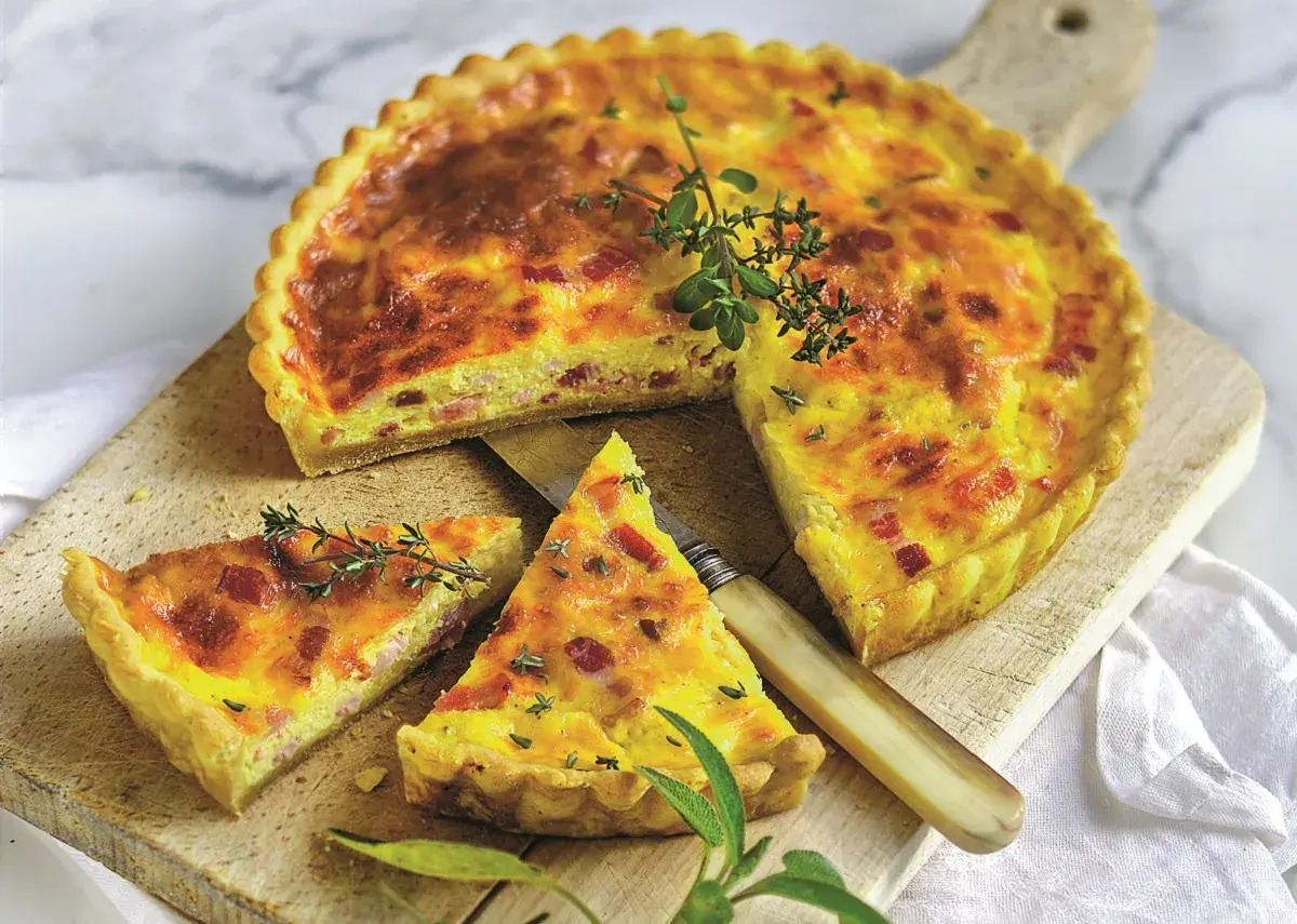 Pyszny quiche lorraine z boczkiem i ziołami, pokrojony na desce, z nożem i gałązkami tymianku.