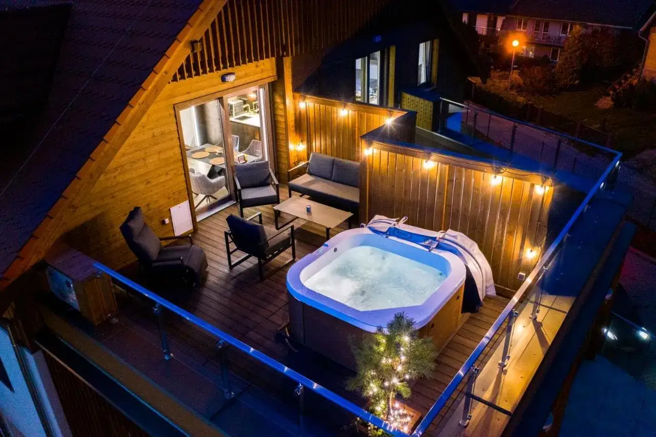 Relaks w jacuzzi na tarasie rezydencji Aqua Szklarska Poręba. Oświetlony taras z meblami i widokiem na noc.