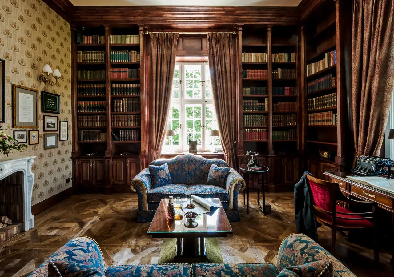 Elegancka biblioteka w pałacu w Ciechocinku. Wygodne sofy, zabytkowa maszyna do pisania i regały pełne książek tworzą atmosferę spokoju i wiedzy.