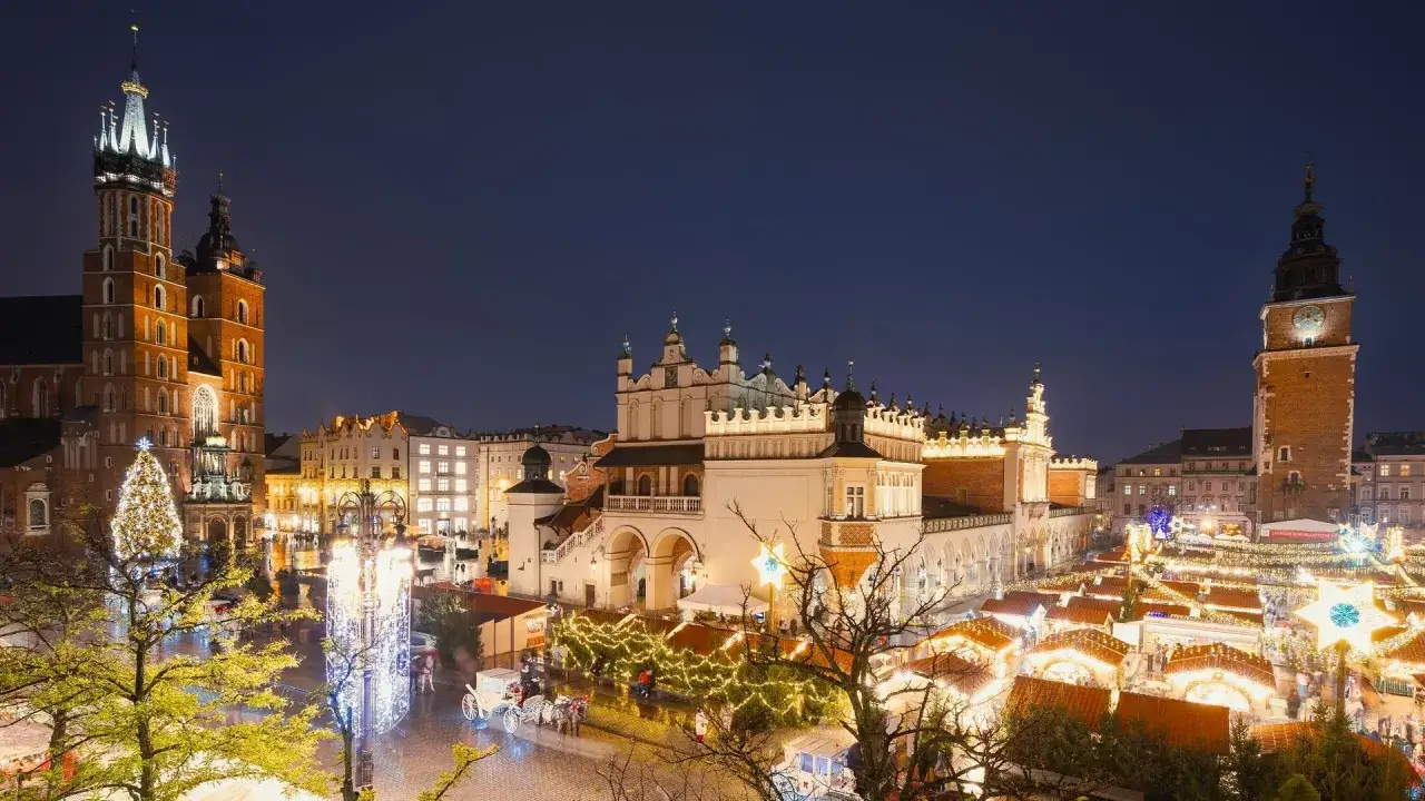 Krak&oacute;w atrakcje zimą: Rynek Gł&oacute;wny nocą, rozświetlony jarmarkiem, choinką i Sukiennicami.