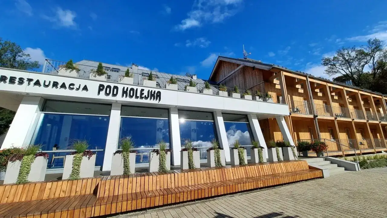 Nowoczesna willa pod kolejką z drewnianą elewacją i restauracją. Wygodna ławka przed budynkiem zaprasza do odpoczynku.
