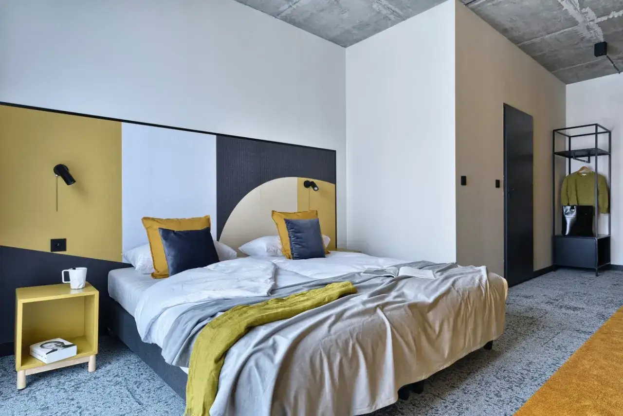 Nowoczesny pokój w arche hotel piła. Dwa łóżka z żółtymi i granatowymi poduszkami, żółty stolik nocny, czarne drzwi i metalowa szafa.
