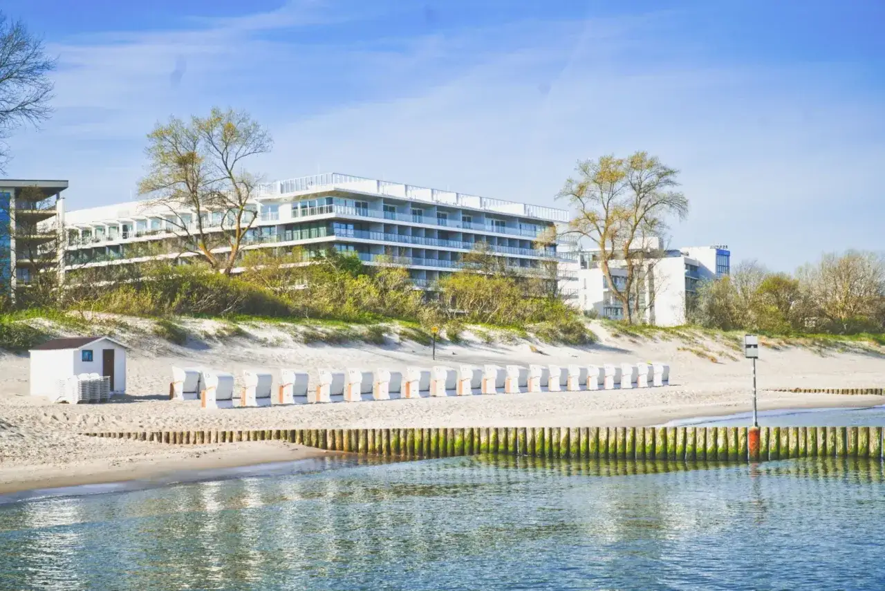 Nowoczesny seaside park hotel z widokiem na plażę i morze. Rząd białych leżaków plażowych czeka na gości.