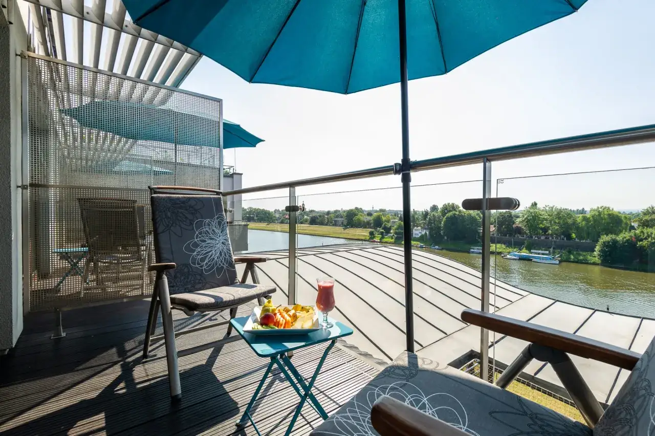 Niebieski parasol i stolik na balkonie hotelowym z widokiem na rzekę. Idealne miejsce na śniadanie w hotelu niebieskim.