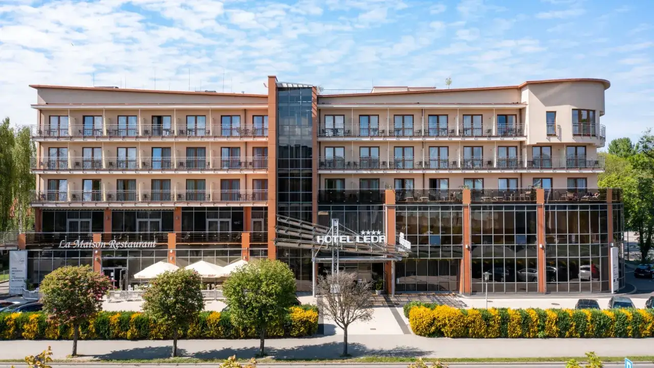 Elegancki hotel Leda Spa z restauracją La Maison, z licznymi balkonami i przeszklonym wejściem, otoczony zielenią.