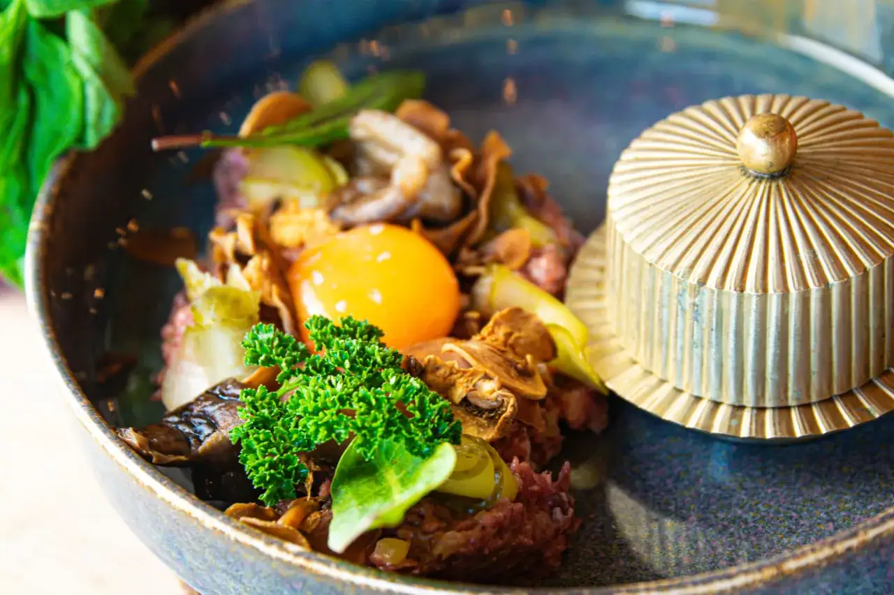Wykwintne danie z tatarem, żółtkiem i ziołami, serwowane w eleganckiej restauracji na Mazurach.
