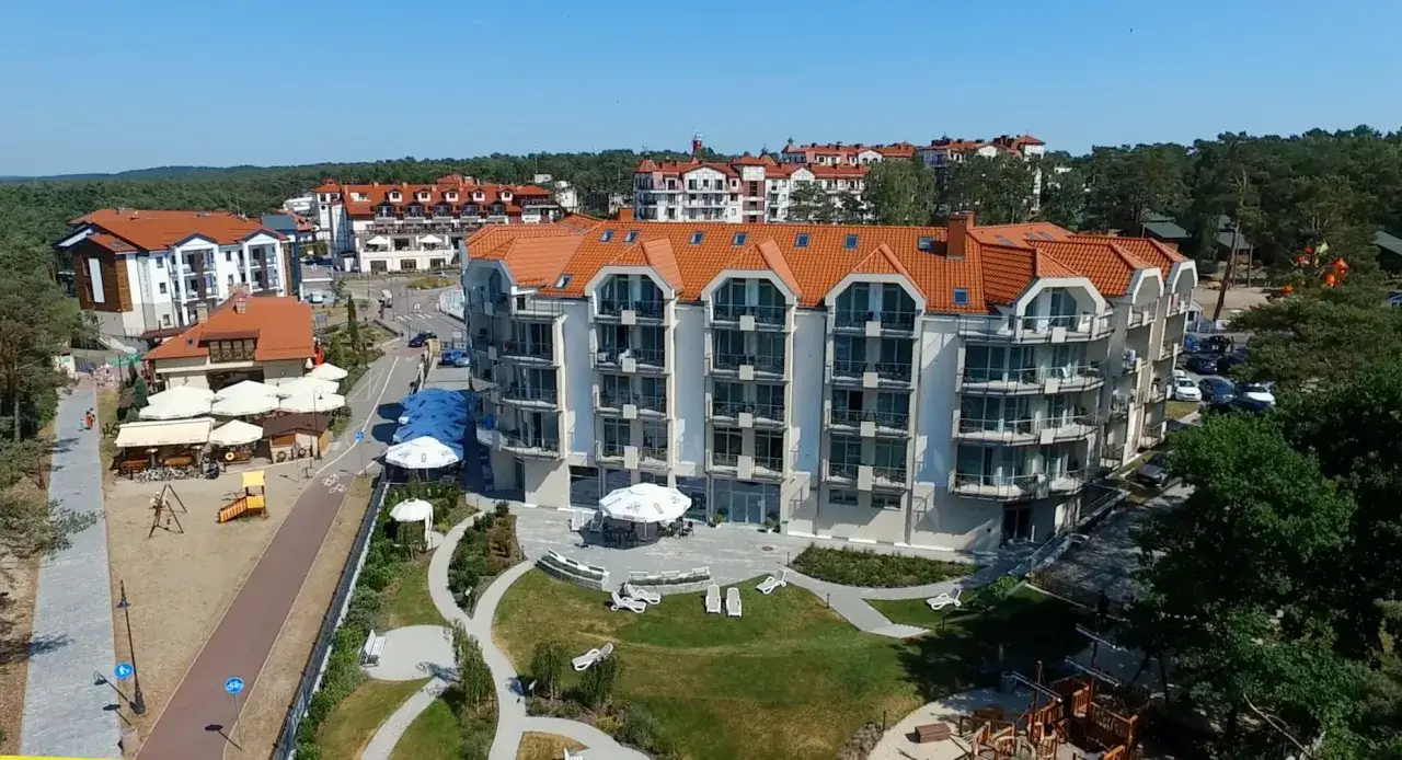 Nowoczesny hotel nat Krynica Morska z widokiem na morze, otoczony zielenią i placem zabaw dla dzieci.