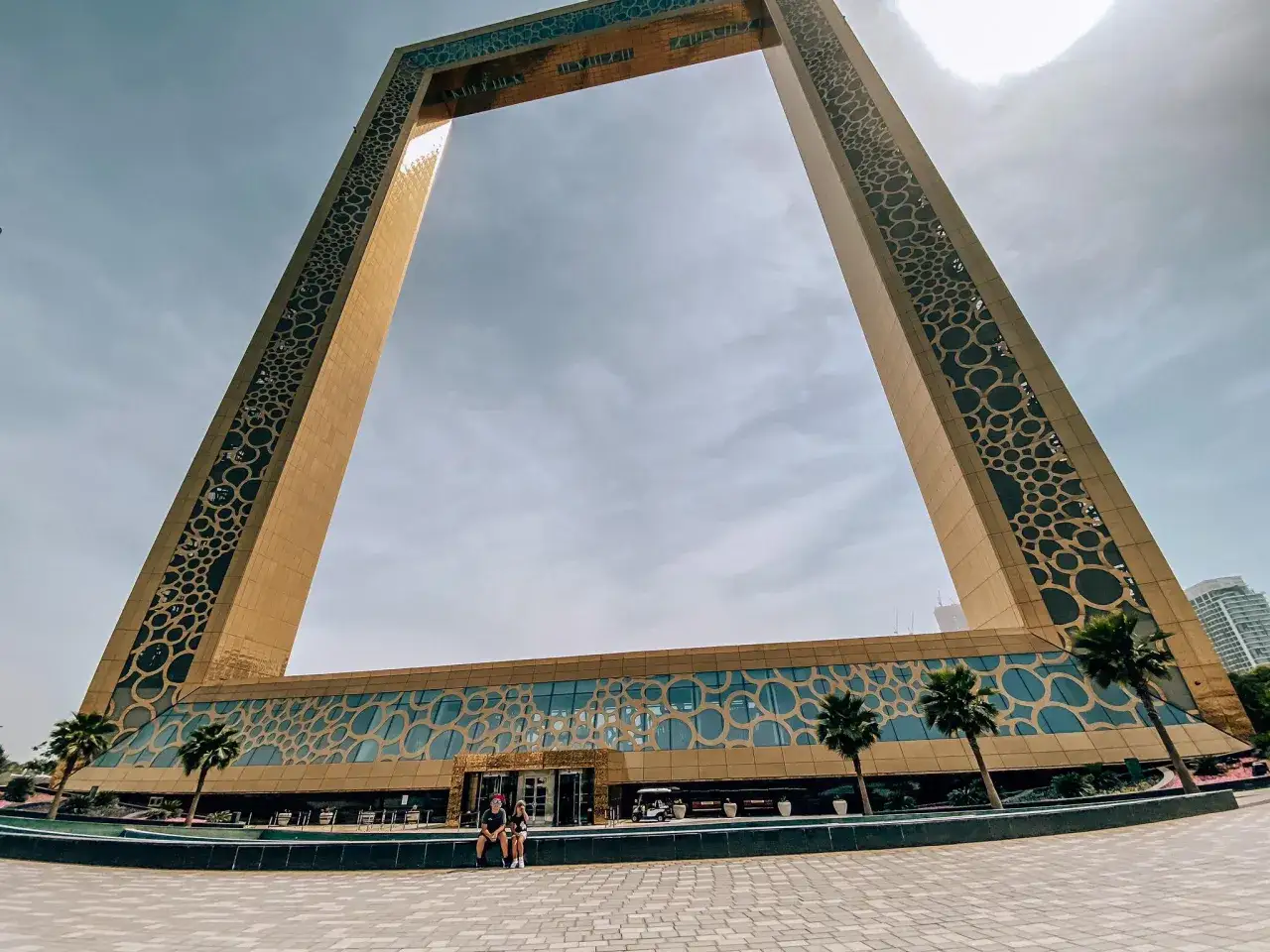 Para młodych ludzi siedzi przed Dubai Frame, jedną z głównych atrakcji Dubaju.