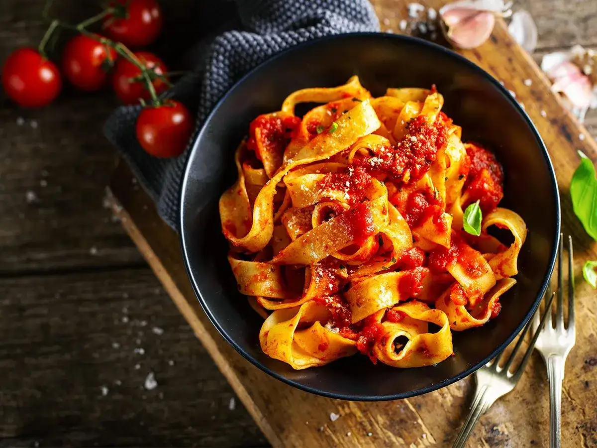 Pappardelle z sosem pomidorowym, świeże pomidory i czosnek na drewnianym blacie. Pyszne dania z pomidor&oacute;w.