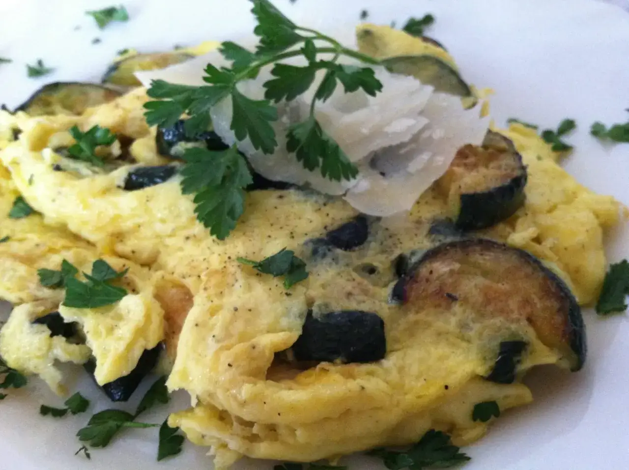 Pyszna frittata z cukinią, udekorowana parmezanem i natką pietruszki. Idealna na lekki posiłek.