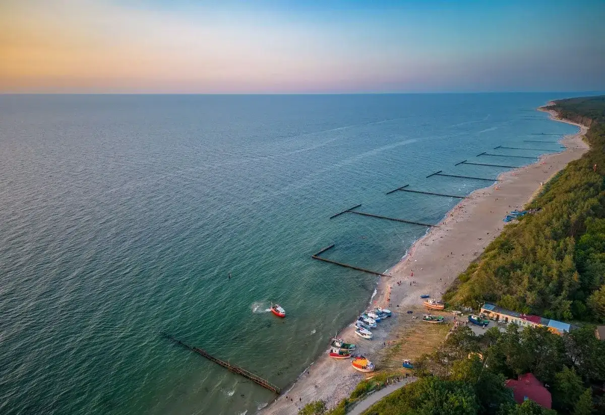 Piękna plaża w Jarosławcu, z łodziami na piasku i falochronami w morzu. Idealne miejsce na wakacyjne atrakcje.