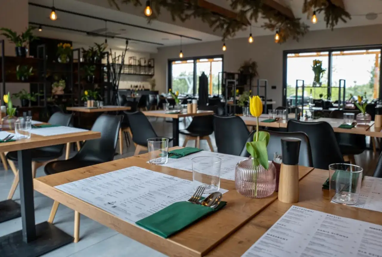Przytulne, klimatyczne restauracje Poznań. Drewniane stoły, czarne krzesła i żółty tulipan tworzą ciepłą atmosferę.