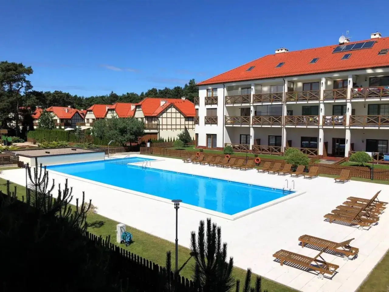 Hotel Shelter Rogowo: basen z leżakami i budynki z czerwonymi dachami w słoneczny dzień.