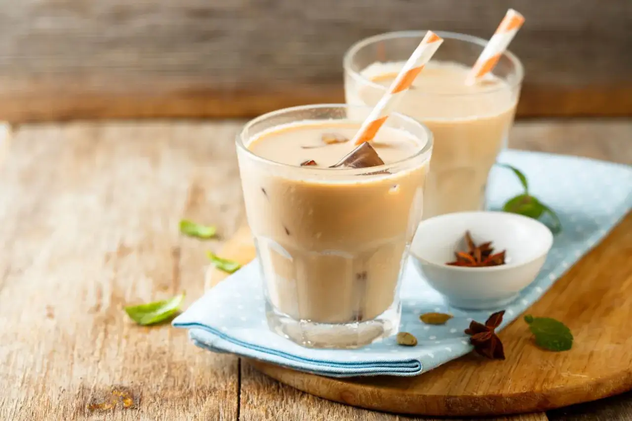 Dwa orzeźwiające chai latte z lodem i słomkami, ozdobione listkami mięty i przyprawami.