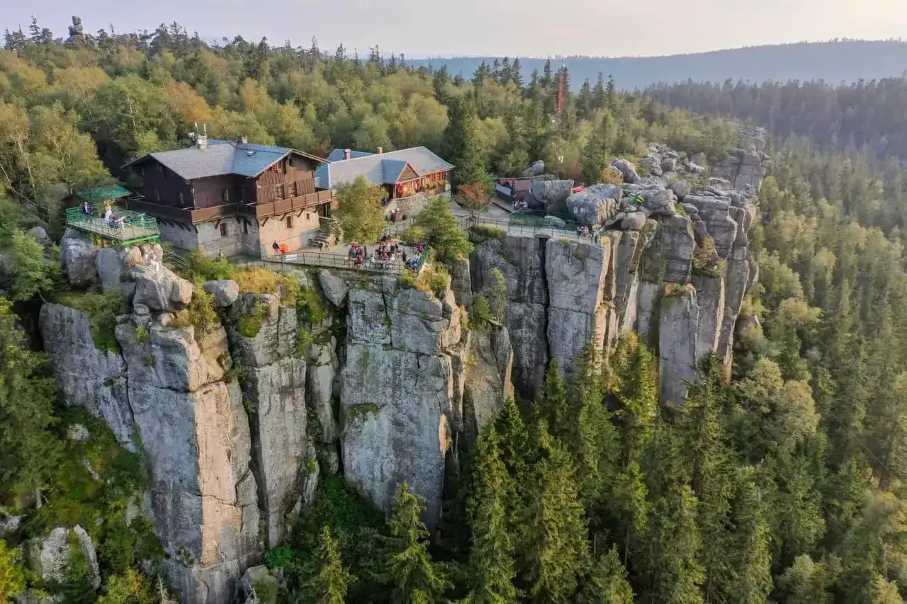 Schroniska w Tatrach na skalistym urwisku, otoczone lasem. Ludzie odpoczywają na tarasach z widokiem na góry.
