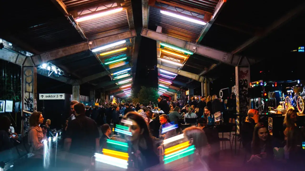 Tętniący życiem nocny market w Warszawie. Kolorowe neony oświetlają tłumy ludzi bawiących się pod zadaszeniem.