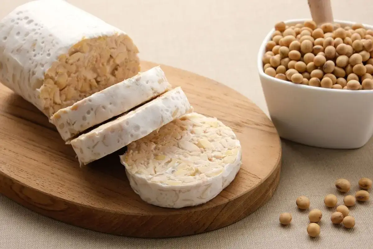 Tempeh co to? Pokrojony blok tempehu na drewnianej desce, obok miseczka z ziarnami soi.