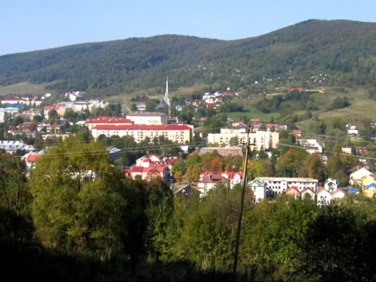 Widok na Ustrzyki Dolne z górami w tle. Miasto z czerwonymi dachami i nowoczesnymi budynkami, otoczone zielenią. Ustrzyki Dolne atrakcje czekają!