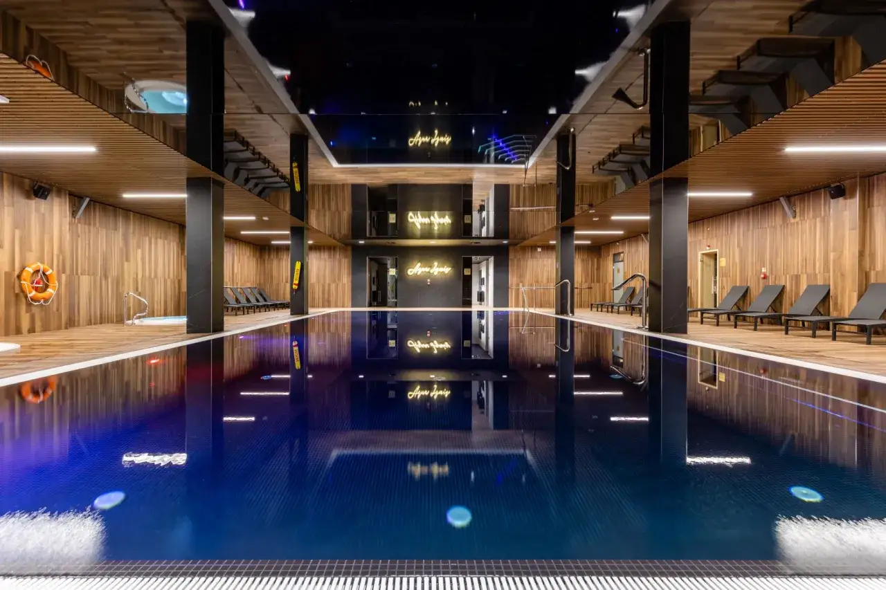 Basen z jacuzzi i leżakami w hotelu w Świeradowie-Zdroju. Eleganckie hotelowe elementy, drewniane wykończenie i neon 